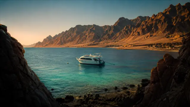Barco en la bahía frente a montañas rocosas al atardecer