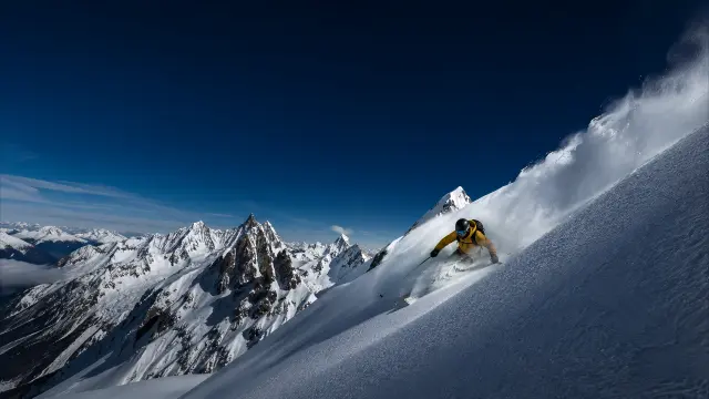 Esquiador en pendiente nevada con montañas al fondo