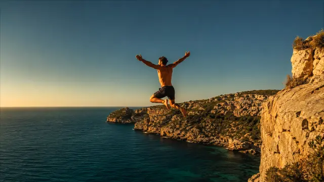 Hombre saltando desde acantilado al mar al atardecer
