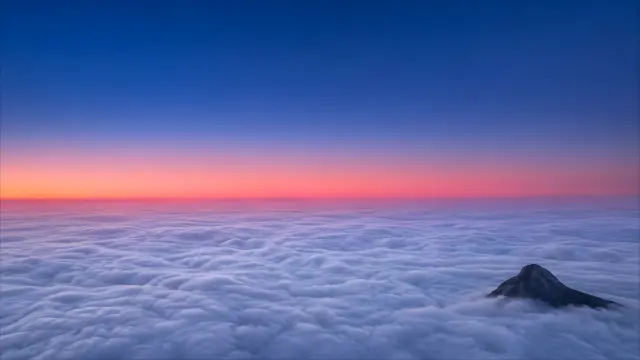 Montaña sobre nubes al amanecer con cielo rosa y azul