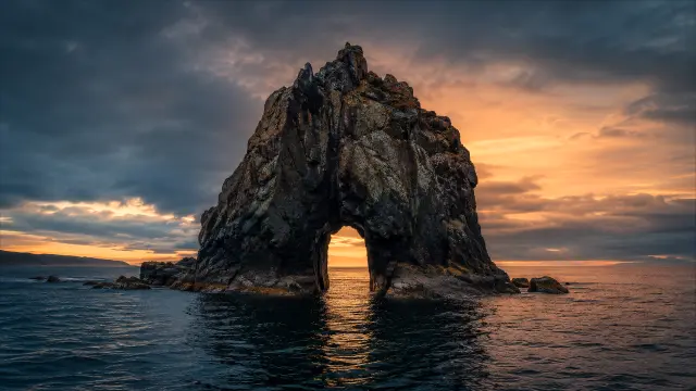 Roca con arco natural al atardecer en el mar