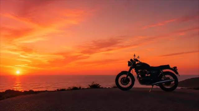 Moto clásica en la costa al atardecer con cielo naranja