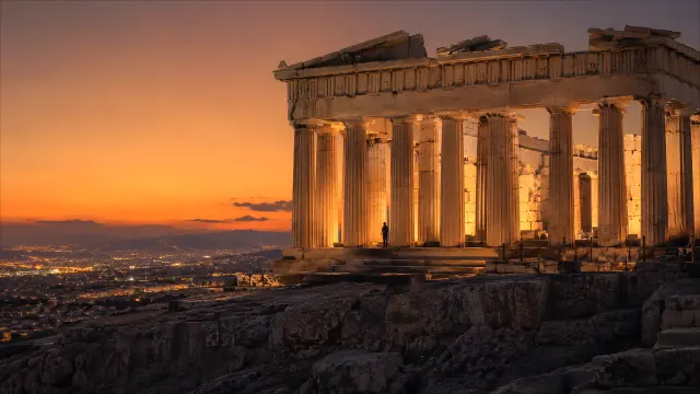 Templo griego al atardecer con vista a la ciudad iluminada