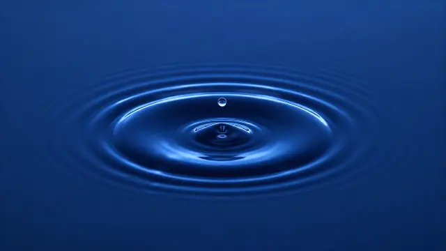 Gota cayendo en agua azul calma con ondas concéntricas